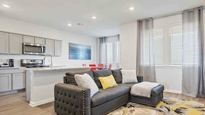 A modern living room with a leather sofa, a coffee table, and a kitchen area in the background. - Charming Retreat 30 Minutes from Vibrant New Orleans - Ideal Short-Term Rental! (Slidell)