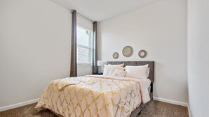 A bedroom with a bed, a nightstand, a window with curtains, and wall-mounted decor. - Charming Retreat 30 Minutes from Vibrant New Orleans - Ideal Short-Term Rental! (Slidell)