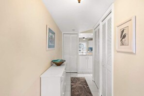A hallway with a white bench, a door with louvered shutters, and a framed picture on the wall.