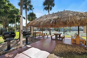 Una terrazza esterna con tetto di paglia, tavoli da picnic e barbecue.