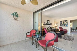 Una sala de estar con muebles de mimbre, un ventanal de vidrio que da a otra habitación y un ventilador de techo.