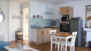 A compact kitchen with a dining area, featuring a stove, oven, refrigerator, and a small sink. - Le 8 ∙ Cosy apartment with sea-view balcony (Mers-les-Bains)