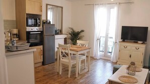 A compact kitchen with a microwave, oven, and refrigerator, a dining area with a table and chairs, and a TV on a cabinet. - Le 8 ∙ Cosy apartment with sea-view balcony (Mers-les-Bains)