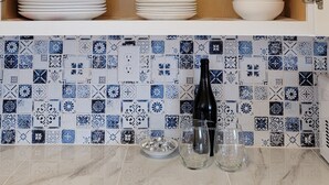 Eine Küche mit einem Holzkabinett, das Glaswaren, Teller und Schüsseln beherbergt. Auf der Arbeitsplatte stehen eine Flasche und Gläser.