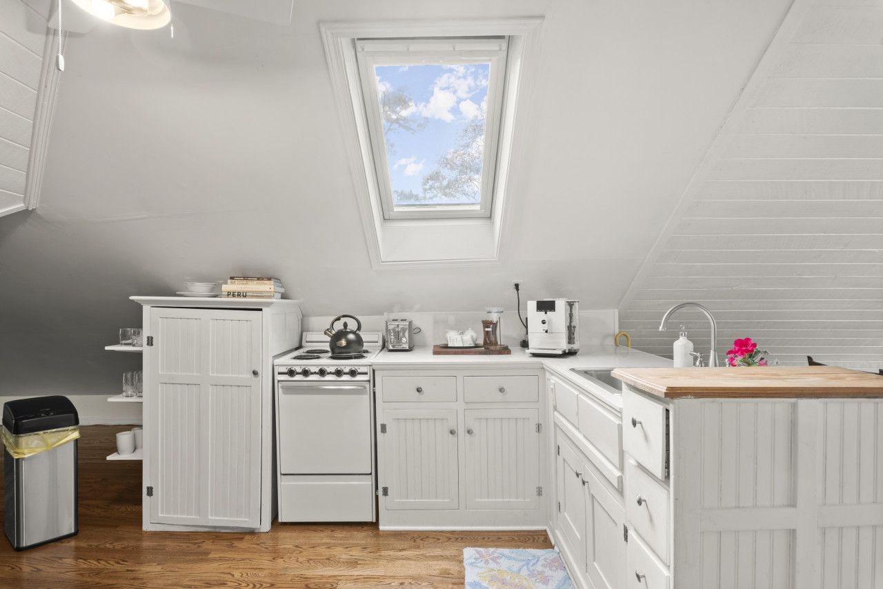 Una cucina compatta con mobili bianchi, un fornello, un lavandino e una finestra con vista sul cielo.