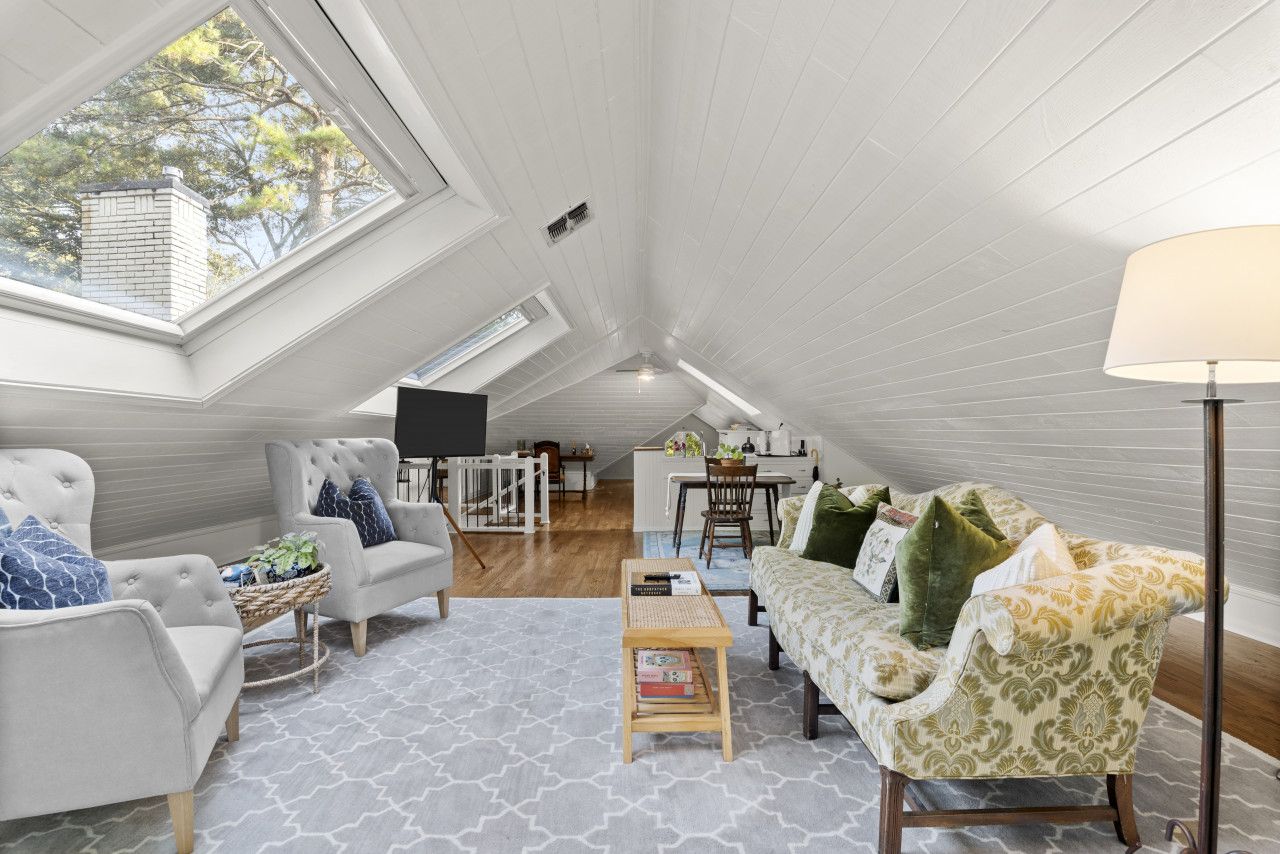 A loft bedroom with a sloped ceiling, a dining area, and a view of trees through a skylight.