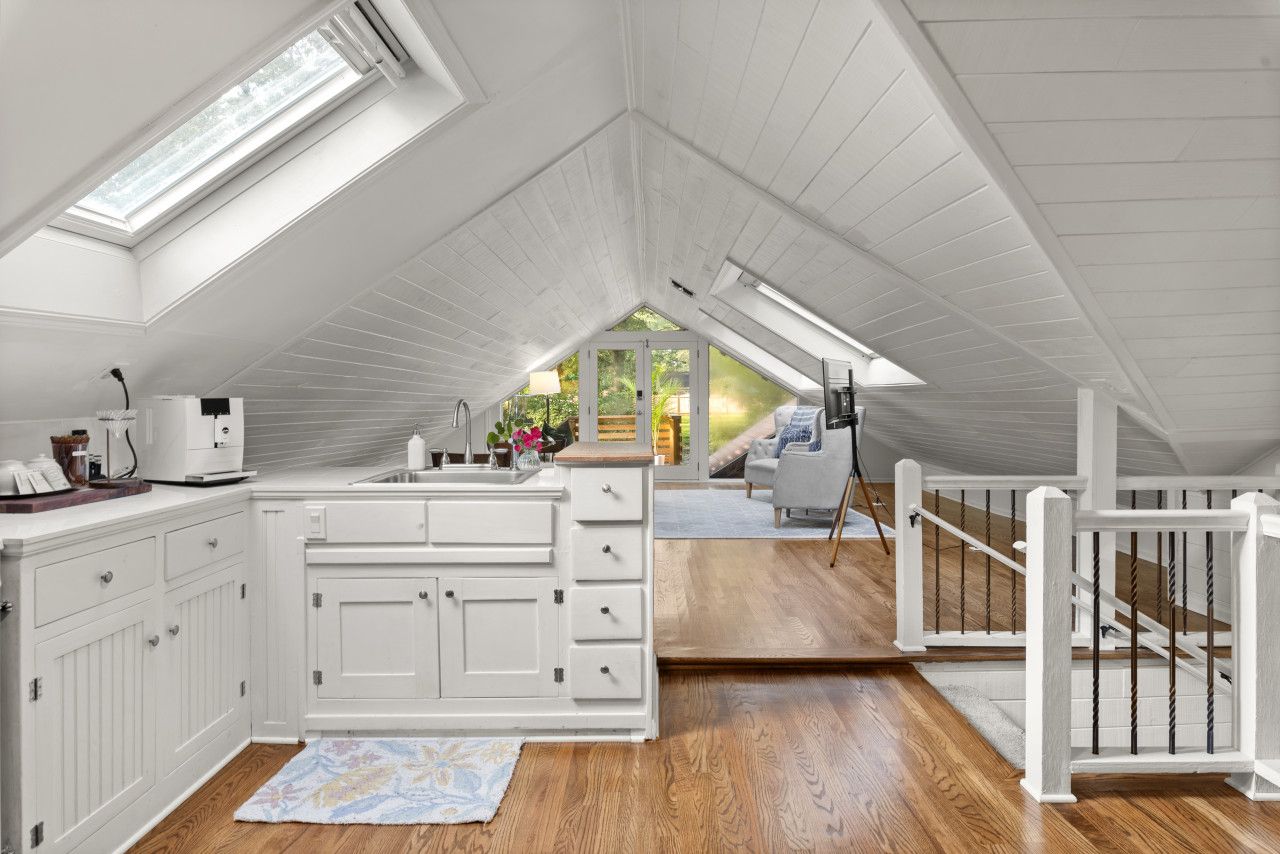 A white attic bedroom with a skylight, wooden flooring, a white dresser, and a view of the outdoors.