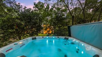A hot tub in a garden with trees and a house in the background.