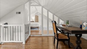 A spacious attic bedroom with a wooden floor, a bed, a desk, and a chair.