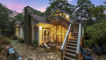 A house with a stone patio, outdoor seating, and a staircase leading to a deck.