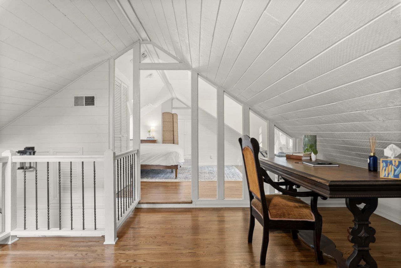 Une pièce avec un plancher en bois, une table à manger avec des chaises, une rambarde blanche et un lit à l’arrière-plan.