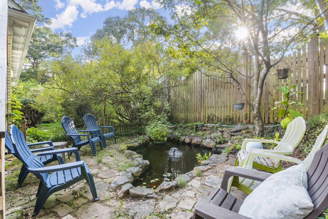 A garden with a pond, wooden fence, and Adirondack chairs.