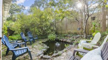 A garden with a pond, wooden fence, and Adirondack chairs.