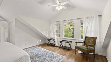 A bedroom with a sloped ceiling, a bed, a window with curtains, a chair, and a patterned rug.