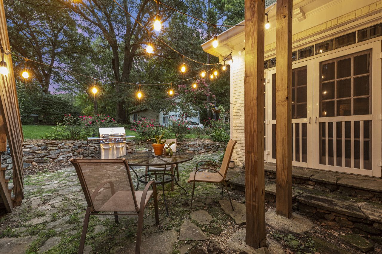 An outdoor patio with a grill, chairs, and string lights.