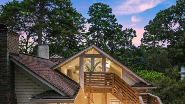 A two-story house with a wooden deck and a staircase leading to a balcony.