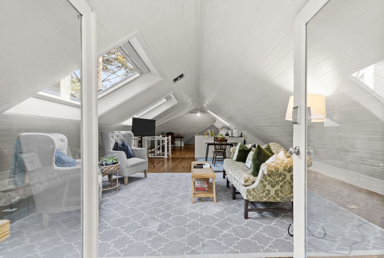 A spacious attic room with a high ceiling, skylights, a dining area, and a cozy seating area with a sofa and armchairs.