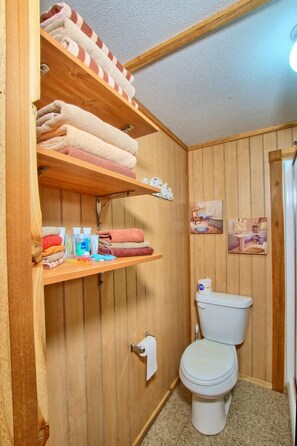 Un bagno con rivestimento in legno, un water, mensole con asciugamani e articoli da toilette.