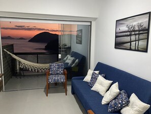 A balcony with a view of the ocean and mountains, a hammock, a blue sofa with patterned cushions, and a framed picture on the wall. - Apartment with spectacular views, Porto Real Resort (Mangaratiba)
