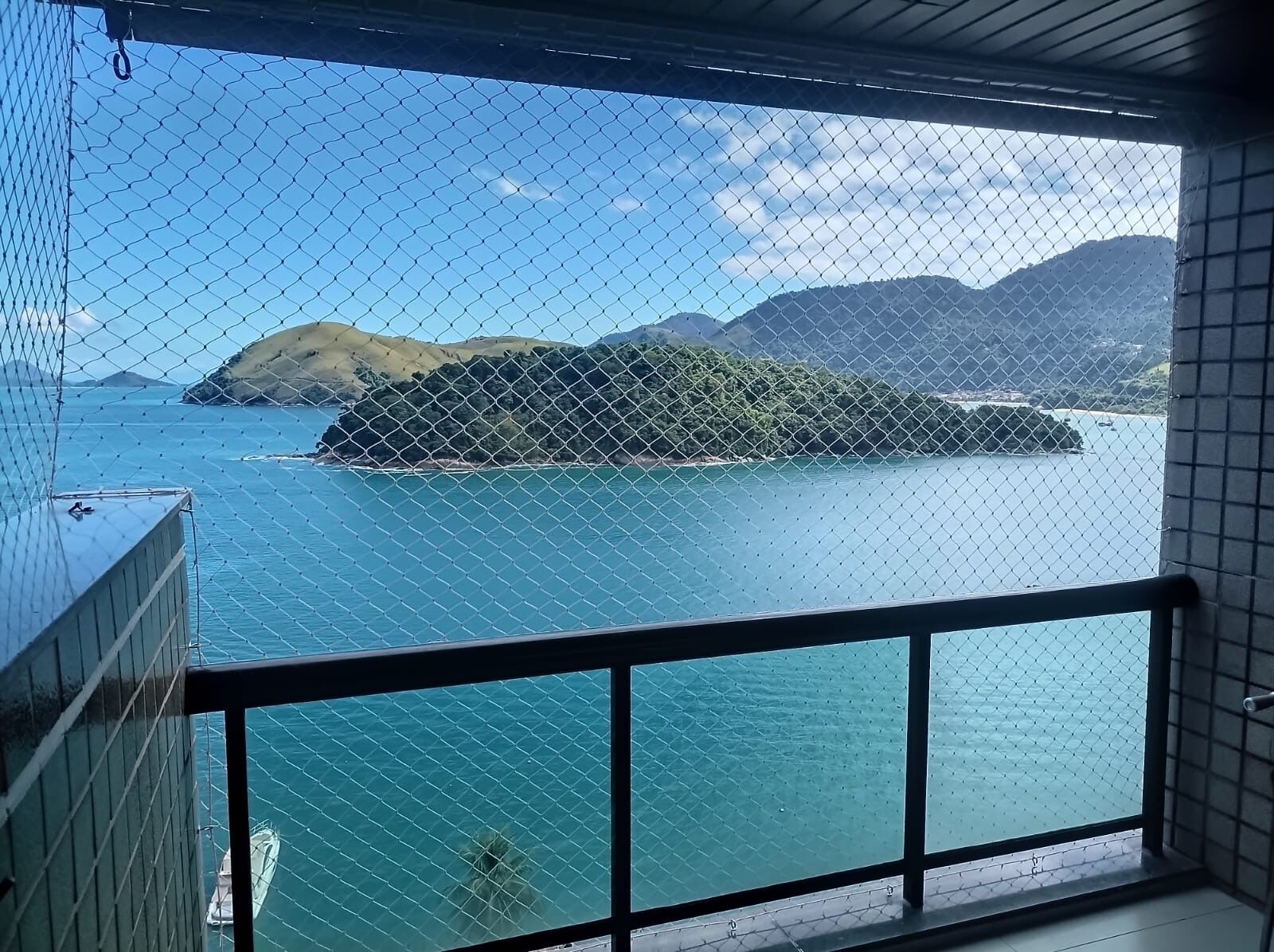 Un balcon offrant une vue sur une mer calme, une petite île et des montagnes lointaines.