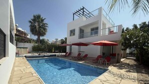 Zwembad met ligbedden en parasols, omringd door een modern gebouw met een witte gevel en een balkon.
