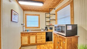 A compact kitchen with wooden cabinets, a built-in microwave, and a window with blinds.
