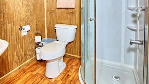 A wooden-paneled bathroom with a shower, toilet, and sink.