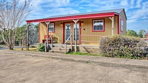 A small, single-story building with a red roof and beige walls, featuring a front porch with steps and a bench.