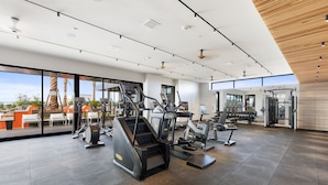 Ein modernes Fitnessstudio mit unterschiedlichen Trainingsgeräten, großen Fenstern und Blick auf Palmen.