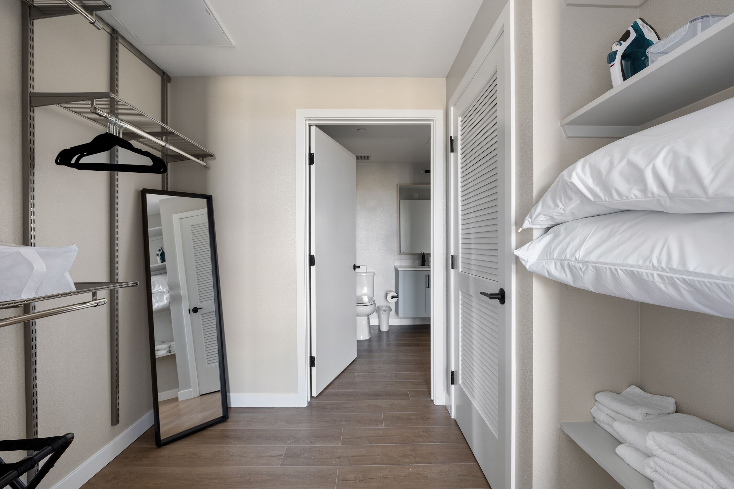 A narrow hallway with a mirrored closet, a hanging rack, and a shelf with folded towels.