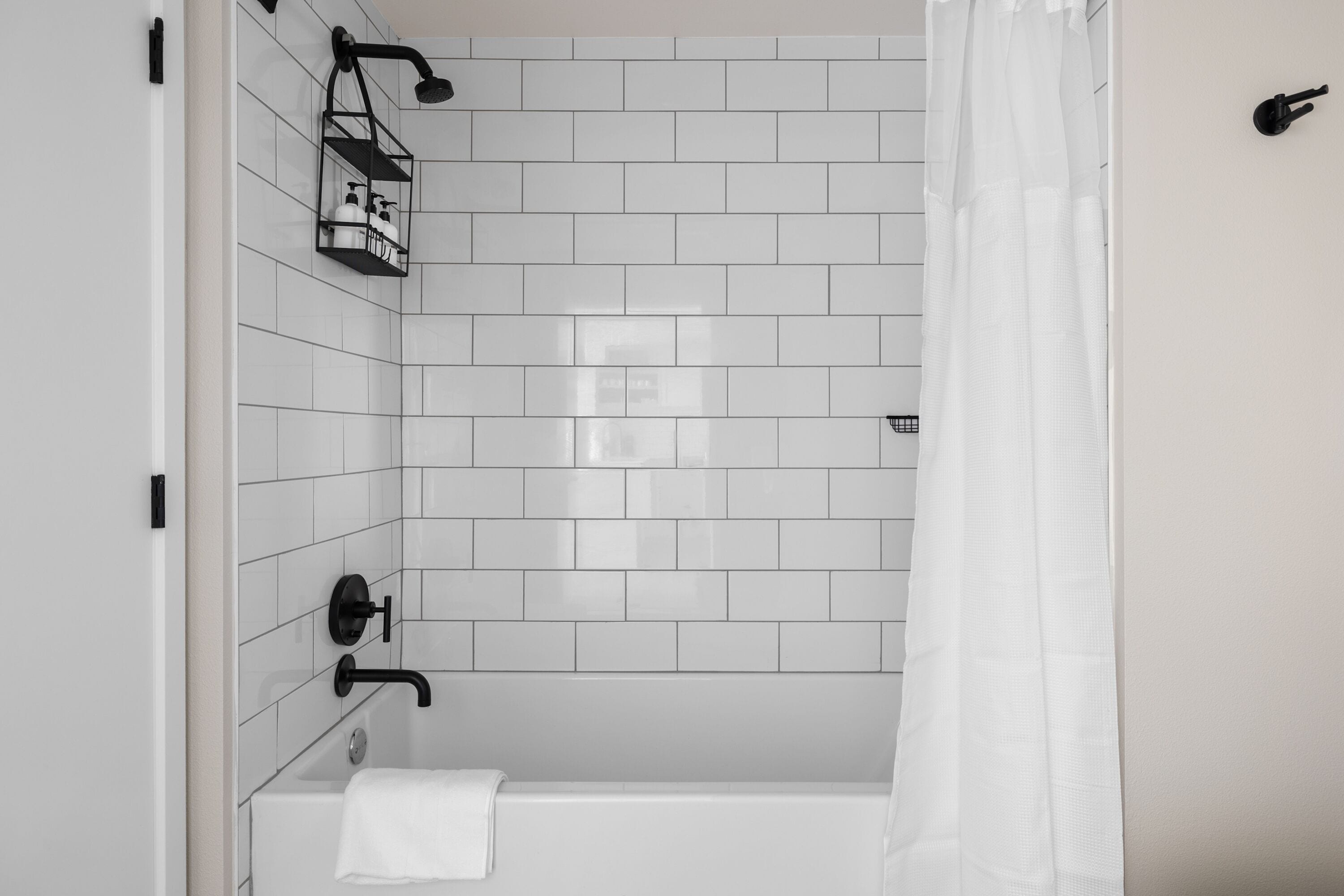 A modern bathroom with white subway tiles, a black showerhead, and a white bathtub.