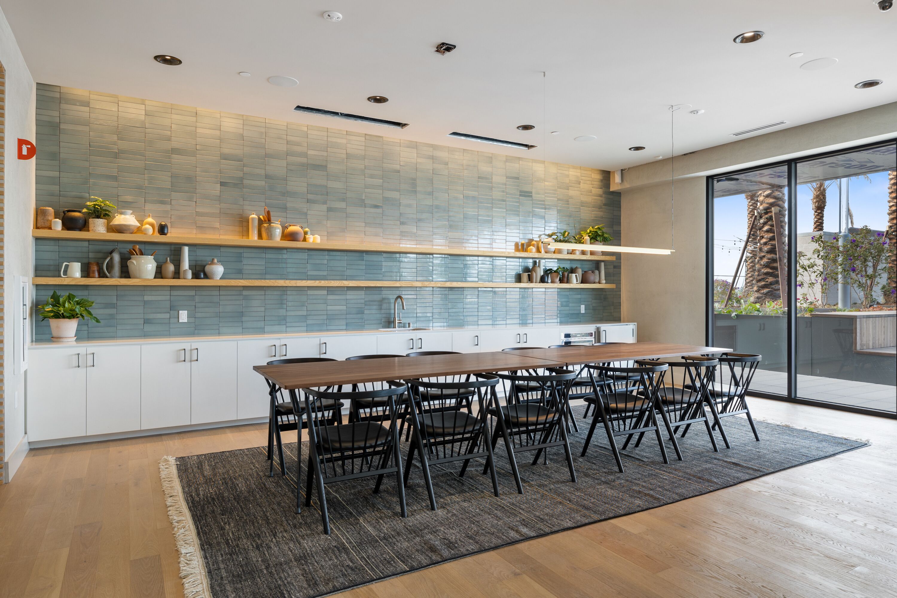 Una cocina moderna con una mesa y sillas de madera, un salpicadero de azulejos y un amplio ventanal con vistas a palmeras.
