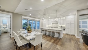Una cocina moderna con armarios blancos, una isla grande con taburetes y un comedor con mesa dispuesta para cuatro.