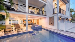 Una casa de dos pisos con piscina, mobiliario exterior y un patio cubierto.