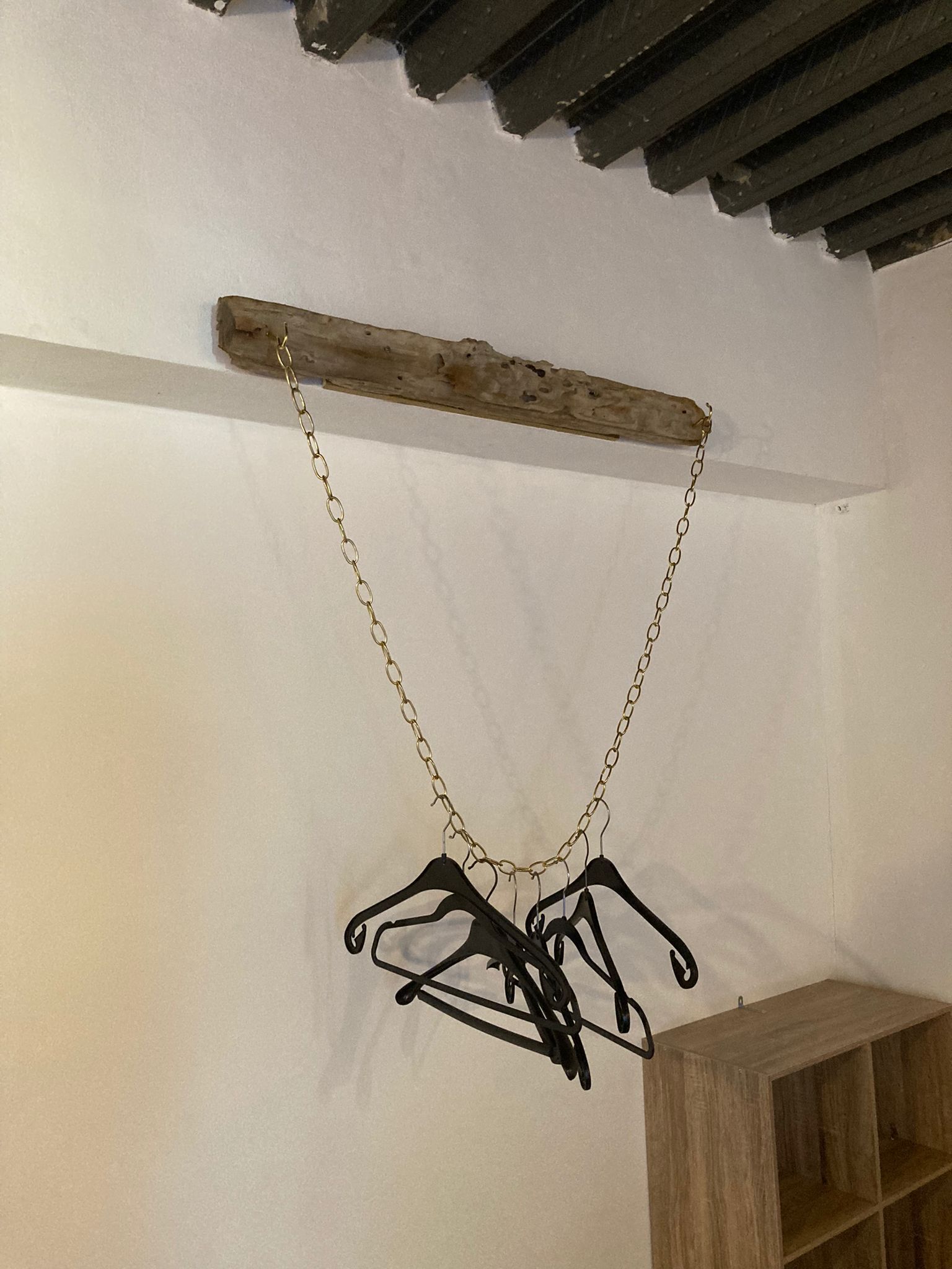 A wooden beam with a gold chain hanging from it, supporting a set of black hangers.