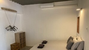 A small, minimalist bedroom with a single bed, a wooden wardrobe, a hanging clothes rack, and a small chest of drawers. - Matua: Spacious `loft style` studio with pool (Willemstad)