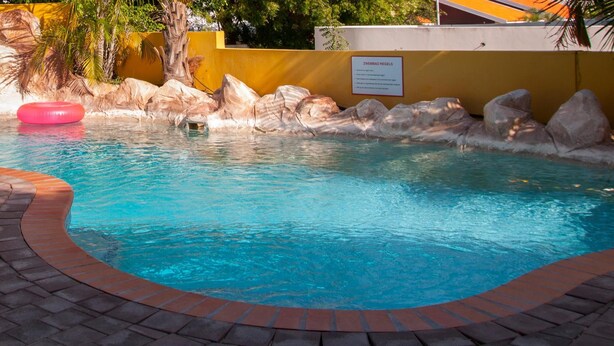 A swimming pool with a brick border, a white lounge chair, and a pink float. - Matua: Spacious `loft style` studio with pool (Willemstad)