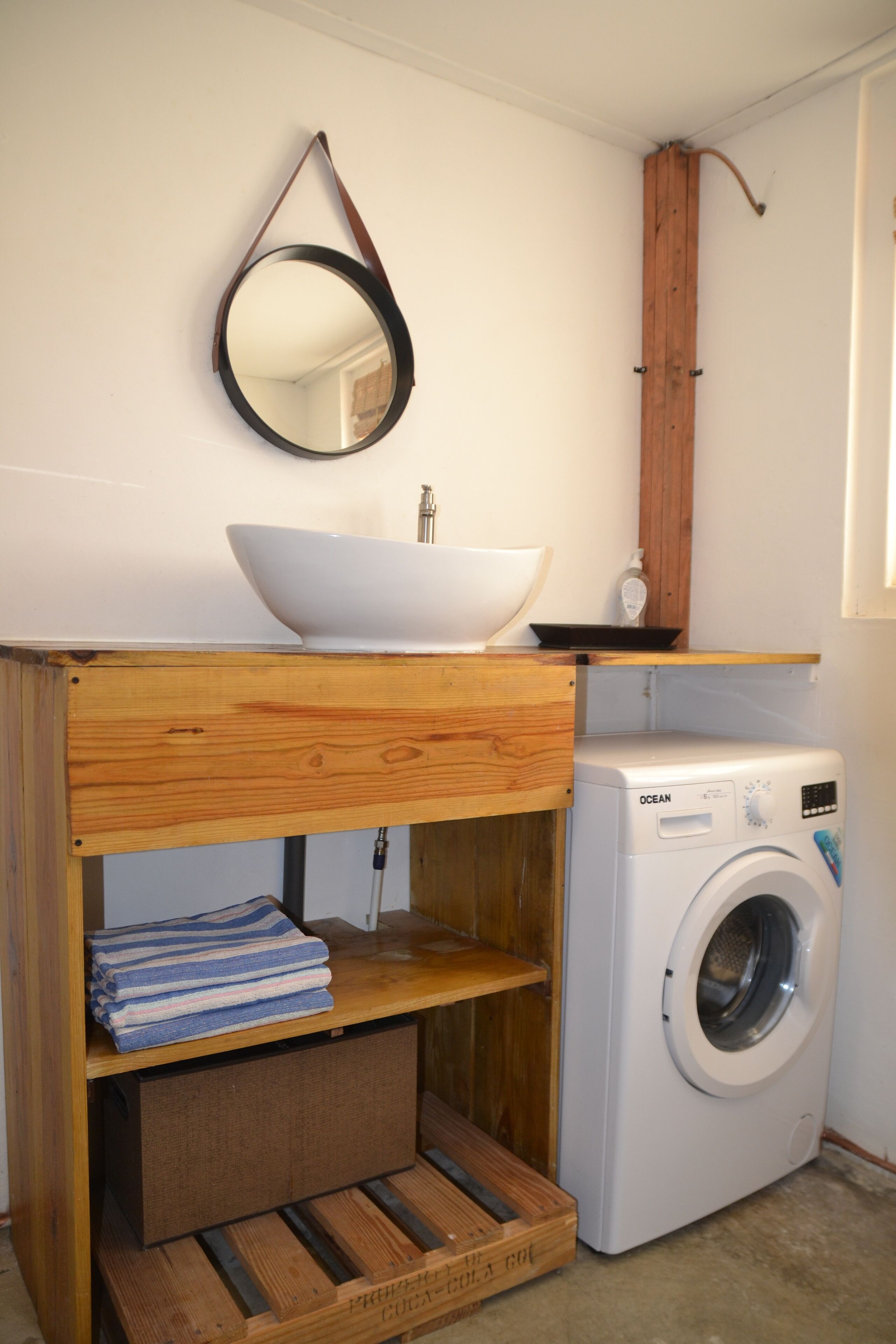 Une petite salle de bain avec un meuble-lavabo en bois, un lavabo blanc, un miroir et un lave-linge à chargement frontal.