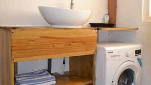 A compact bathroom with a wooden vanity, a white sink, a mirror, and a front-loading washing machine. - Matua: Spacious `loft style` studio with pool (Willemstad)