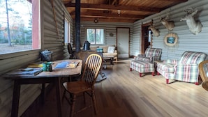 Interior de uma cabana de toras com área de refeições, um sofá, poltronas xadrez e chifres de veado na parede.