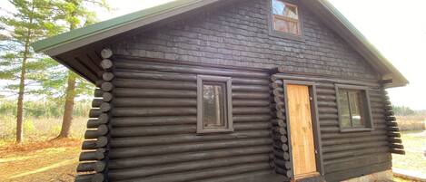 Une cabane en rondins avec une porte en bois, deux fenêtres et une véranda.