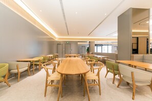 A spacious indoor area with multiple wooden tables and chairs, a large central table, and a seating area with sofas.