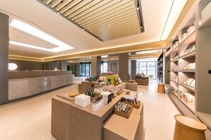 A modern hotel lobby with a reception desk, seating area, and bookshelves. - Ji Hotel (Shanghai)