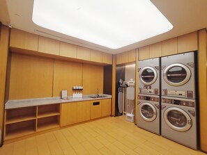 A modern laundry room with wooden cabinets, a sink, and multiple washing machines.
