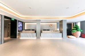 A modern hotel lobby with a reception desk, digital information screen, and a large potted plant. - Ji Hotel (Shanghai)