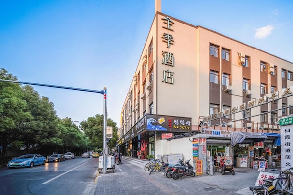 A building with a sign that reads '全季酒店' indicating a hotel. There are bicycles parked outside, and a street with cars and a pedestrian crossing. - Ji Hotel (Shanghai)