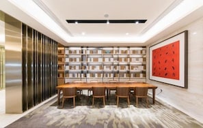 A modern dining area with a long wooden table, chairs, a patterned carpet, and a bookshelf with books. - Ji Hotel (Shanghai)