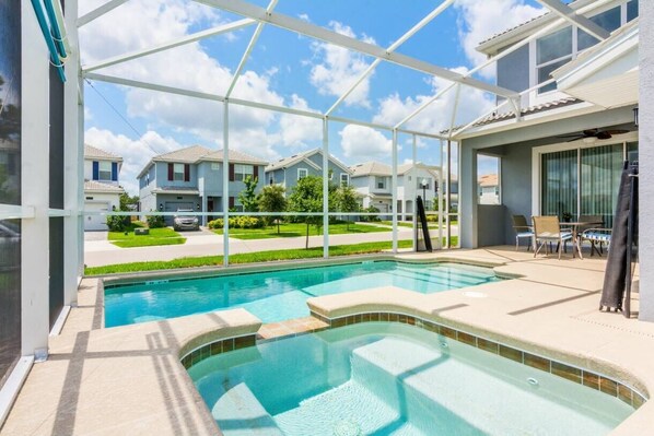 A swimming pool with a glass enclosure, surrounded by a patio area with chairs and a table. - Modern 5BR/5BA Vacation Home with Private Pool CG1593 (Davenport)