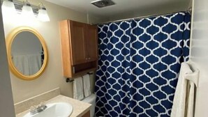 Une salle de bain avec un lavabo blanc, des meubles en bois, des toilettes et un rideau de douche à motifs géométriques.