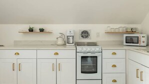 A kitchen with white cabinets, gold handles, a stove, a coffee maker, and a microwave.